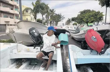  ?? Felix Marquez Associated Press ?? A TOURIST boat operator bails water in Veracruz, Mexico, after moving his boat onto land as a precaution.