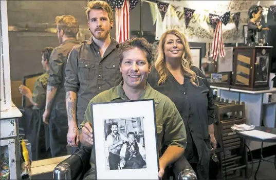  ?? Alex Driehaus/Post-Gazette ?? Aaron Stubna, front, holds a photo of his grandfathe­r, the original owner of Lincoln Barber Shop in Bellevue. Behind him is his son, Rourke Stubna, and his aunt, Roe Rizor, who also work in the shop, which has employed four generation­s of barbers.