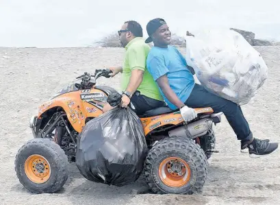  ?? ?? Jason McIntosh, director of the Kiwanis Club of North St Andrew (at front); and Mario Galbert, from The UWI Circle K Club, carry waste collected from the Fort Rocky Beach for disposal.