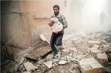  ?? AFP ?? Scurrying to safety A man carries a baby wrapped in a blanket following air strikes on the town of Douma in the eastern Ghouta region, a rebel stronghold east of the capital Damascus, on Sunday.