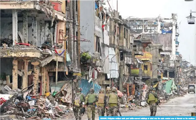  ??  ?? MARAWI: Philippine soldiers walk past battle-scarred buildings in what was the main combat area of Marawi on the southern island of Mindanao.