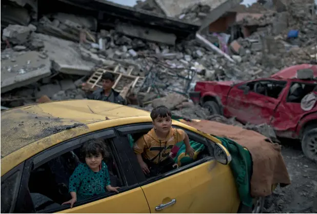  ?? AP ?? CAUGHT iN THE CROSSFIRE: Children play inside a damaged car in a neighbourh­ood recently retaken by Iraqi security forces from Daesh militants on the western side of Mosul. —