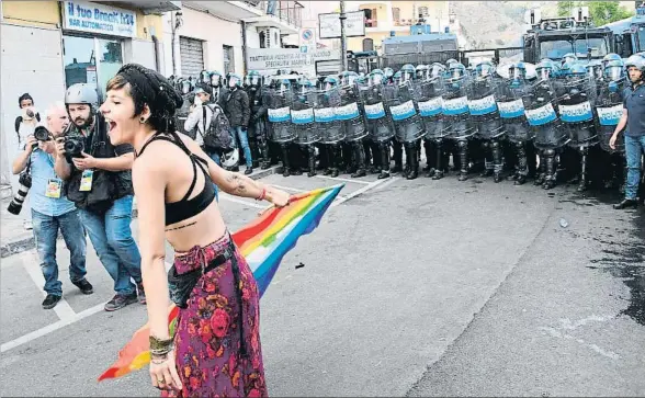  ??  ?? Una manifestan­te ondea una bandera arco iris frente a los antidistur­bios en Giardini Naxos, cerca de Taormina