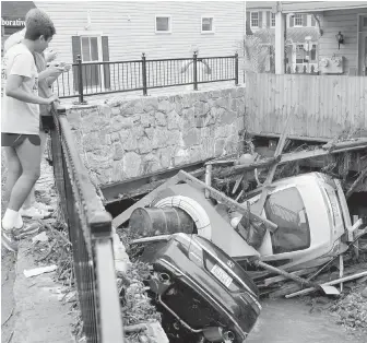  ?? DAVID MCFADDEN, AP ?? Residents examine cars Monday left crumpled in a tributary of the rain-swollen Patapsco River that burst its banks and channelled through Main Street in Ellicott City, Maryland.