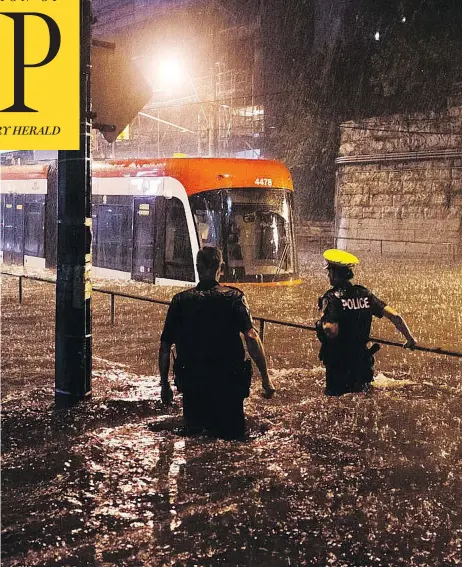  ?? SHLOMI AMIGA / THE CANADIAN PRESS ?? Toronto police officers look on as water floods King Street West, stopping a streetcar in its tracks on Tuesday.