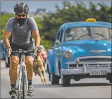  ??  ?? A cyclist carries a chicken while he pedals his bicycle in Havana.