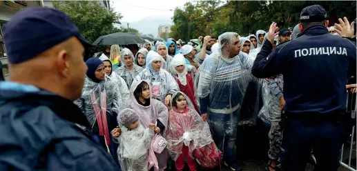  ??  ?? Sotto la pioggia Un poliziotto serbo dà istruzioni a migranti in fila per la registrazi­one in un campo profughi a Presevo, nel Sud della Serbia
(Ap/Darko Vojinovic)