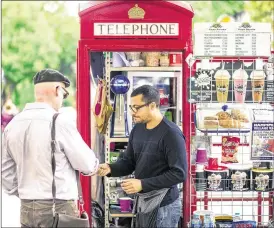  ?? MILES WILLIS / BLOOMBERG ?? Umar Khalid, co-owner of the Kape Barako telephone box coffee stall, serves a customer on Hampstead High Street in London.