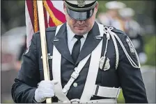  ??  ?? A Columbus police officer carries an American flag as he arrives with the Color Guard before the burial at St. Joseph Catholic Cemetery.