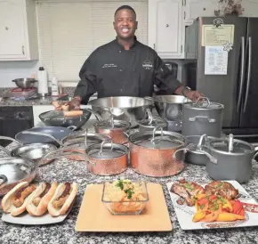  ?? MICHAEL SEARS / MILWAUKEE JOURNAL SENTINEL ?? Former Packer LeRoy Butler poses in his kitchen with some of his favorite dishes and cookware. From left are his LeRoy Leaps Green ‘n Gold Game Day Brats, 5-cheese Creamy Mac’n Cheese and Rosemary Pork Chops.
