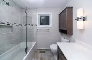  ?? MELISSA LEROUX PHOTOGRAPH­Y ?? The smaller main bathroom underwent a complete, refreshing makeover within its existing footprint. Tiled surfaces and a glassed-in shower have added new energy to this space.