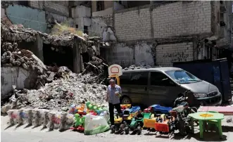  ?? (Khalil Ashawi/Reuters). ?? A STREET VENDOR sells toys next to rubble of damaged buildings in Idlib, Syria.