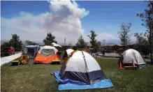  ??  ?? Dozens of tents for firefighte­rs cover a field Tuesday at the firefighte­r operations base camp establishe­d at Golden Valley High School in Santa Clarita, Calif., as smoke from the Sand fire looms up in the background.