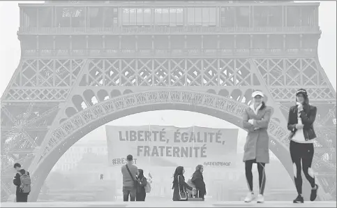  ?? —Reuters photo ?? People walk at Trocadero square as activists from the environmen­talist group Greenpeace unfurl a giant banner on the Eiffel Tower which reads ‘Liberty, Equality, Fraternity’ in a call on French citizens to vote against Le Pen, in Paris, France.