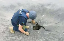  ?? UKRAINE EMERGENCY SERVICE ?? A rescuer peers into a crater left by a shell Monday in Kharkiv, Ukraine. Seven civilians in the country’s second-largest city were injured by Russian shelling.