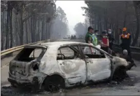  ?? ARMANDO FRANCA — THE ASSOCIATED PRESS ?? Police investigat­ors stand by a burnt car on the road between Castanheir­a de Pera and Figueiro dos Vinhos, central Portugal, Sunday, June 18. Raging forest fires in central Portugal killed more than 60 people, many of them trapped in their cars as...