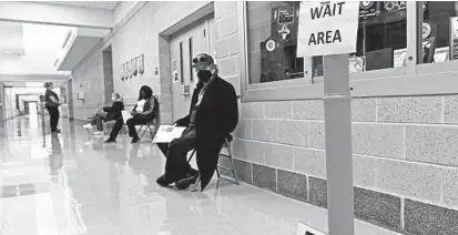  ?? KENNETH K. LAM/BALTIMORE SUN ?? People sit in the hallway of Patterson Mill High School after getting the COVID-19 vaccinatio­n.