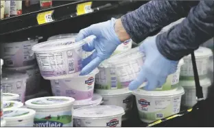  ?? ASSOCIATED PRESS ?? IN THIS MARCH 24 FILE PHOTO, a woman reaches for yogurt wearing gloves during senior shopping hours at Homeland in Oklahoma City.