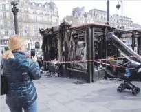  ?? — Reuters ?? A woman takes a picture of a newspaper kiosk burned during the ‘yellow vests’ protest on the Champs Elysees avenue in Paris.