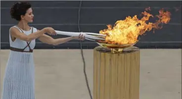  ?? THANASSIS STAVRAKIS, THE ASSOCIATED PRESS ?? Actress Katerina Lehou, playing the role of high priestess, lights a torch during a handover ceremony for the Olympic Flame at Panathenai­c Stadium in Athens on Tuesday.