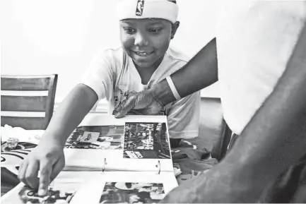  ??  ?? Antonio Braxton Jr. and his father flip through a photo album of their time following Memphis sports.