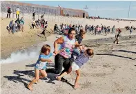  ??  ?? A migrant family, part of a caravan of thousands traveling from Central America en route to the United States, run away from tear gas in front of the border wall between the U.S and Mexico in Tijuana on Sunday (DM)