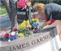  ?? PHOTO BY NATE BILLINGS, THE OKLAHOMAN ?? Katrina Prince, of Norman, places flowers Sunday on the statue of James Garner on Main Street in downtown Norman. Garner died Saturday at age 86.