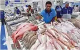  ??  ?? Pakistani kushti wrestler Mohammed Arsalan (center), also known as Kala Pehlwan, working at the fish market in Dubai.