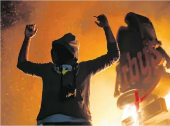  ?? FOTO: JOHN MINCHILLO/DPA ?? Ein Demonstran­t hält die Arme nach oben neben einem brennenden Fast-Food-Geschäft in Minneapoli­s. Nach der Tötung von George Floyd kam es in mehreren US-Städten zu Protesten und Ausschreit­ungen.