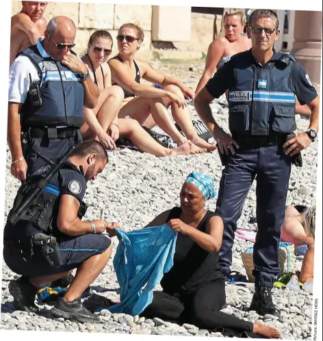  ?? Picture:VANTAGENEW­S ?? Stripped of her dignity: Police take down the woman’s details as she takes off her shirt on a beach in Nice