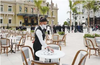  ?? AFP PHOTO ?? A waiter wearing a protective facemask sets a table on the terrace at the Cafe de Paris as restaurant­s and cafes reopen in the newly inaugurate­d Casino place on Monaco, on June 2, 2020, as the Principali­ty eases lockdown measures taken to curb the spread of the Covid-19.
NEW YORK: