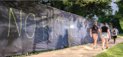  ?? TYLER PASCIAK LARIVIERE/SUN-TIMES FILES ?? Festivalgo­ers walk by graffiti that reads “NO RIOT FEST IN OUR PARK” along the fence in Douglass Park last September.
