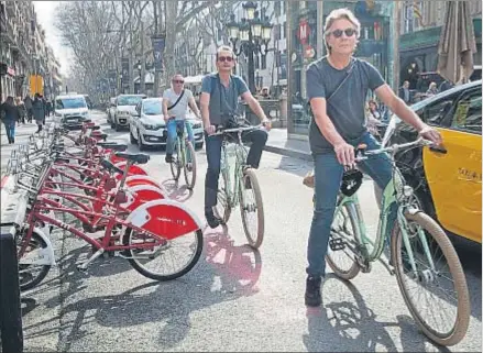  ?? KIM MANRESA ?? Tres turistas con bicicletas de alquiler pasando junto a una estación del Bicing, ayer, en la Rambla