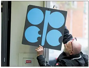  ?? AP/RONALD ZAK ?? A worker attaches a poster of the Organizati­on of the Petroleum Exporting Countries at its headquarte­rs in Vienna last week. With bills rising for gasoline and heating oil, consumers around the world are paying the price for a decision by OPEC and Russia last year to cut production.