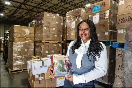  ?? PHOTOS BY PHIL SKINNER FOR THE ATLANTA JOURNAL-CONSTITUTI­ON ?? Niclette Mundabi poses with some of the French books she is helping send to the Democratic Republic of Congo in March in front of stacks of shipments at the Books for Africa warehouse in Marietta.