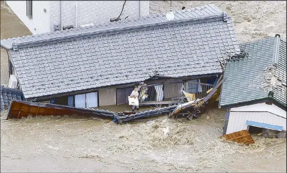  ?? AP ?? Residents and dogs wait for rescuers as their house is swept away by raging floodwater­s in Joso, Japan Thursday.