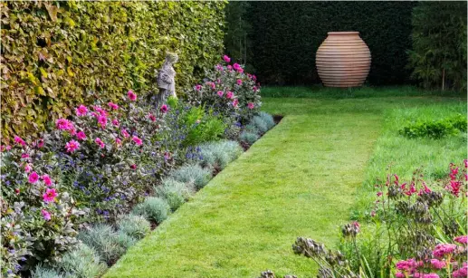  ??  ?? POINT OF PERSPECTIV­E Straight lines bring a formal feel and a sense or order. Here, a grass path leads the eye to a focal point at the end of the garden – a shapely terracotta urn – which is highlighte­d against a dark hedge. A statue stands amid Dahlia ‘Roxy’, regular clumps of dianthus and Caryopteri­s x clandonens­is ‘Kew Blue’, enhancing the sense of classic calm