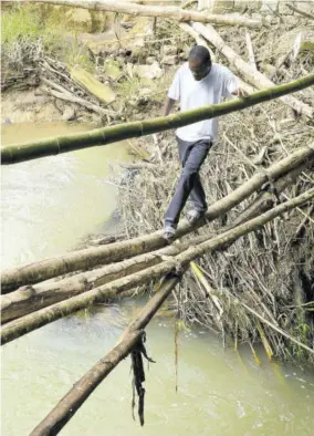  ?? (Photo: Karl Mclarty) ?? A Cowick Park resident walking on a makeshift footbridge to cross the river at Troy after the bridge collapsed in 2021.