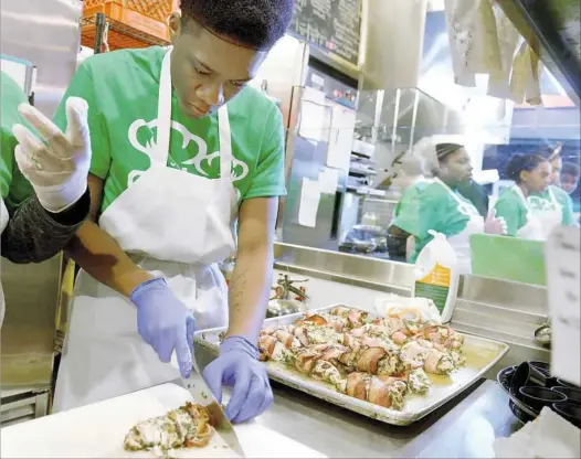  ?? Pam Panchak/Post-Gazette photos ?? Donyae Taylor, with CISP North, cuts up bean-wrapped herb chicken breast for tasting samples Saturday during the Project Lunch Tray competitio­n at Smallman Galley in the Strip District. The competitio­n, an initiative of Community Kitchen Pittsburgh and...