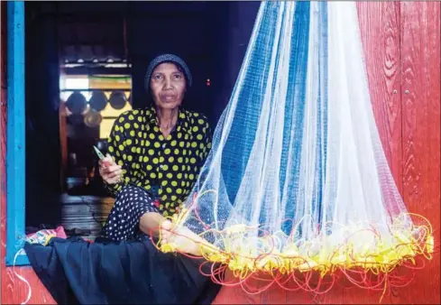  ?? ATHENA ZELANDONII ?? A woman repairs a fishing net at a village in Koh Kong province that has been affected by years of sand dredging.