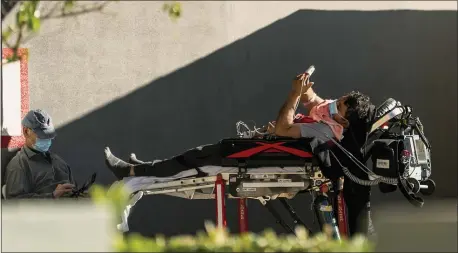  ?? DAMIAN DOVARGANES — THE ASSOCIATED PRESS ?? An unidentifi­ed patient uses his mobile phone while receiving oxygen on a stretcher, as Los Angeles Fire Department Paramedics monitor him outside the Emergency entrance, waiting for his room at the CHA Hollywood Presbyteri­an Medical Center in Los Angeles Friday, Dec. 18, 2020.