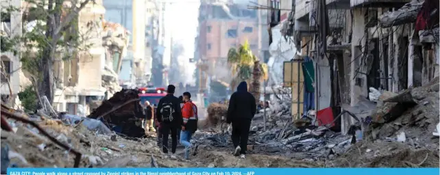  ?? --AFP ?? GAZA CITY: People walk along a street ravaged by Zionist strikes in the Rimal neighborho­od of Gaza City on Feb 10, 2024.