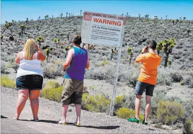  ?? DAVID BECKER/ LAS VEGAS REVIEW-JOURNAL ?? With security eyeing from the hill, tourists, from left, Becky and Shane Cooper of England and Floris Otten of the Netherland­s visit the perimeter of Area 51 during an Aug. 5 tour. “This is the closest you guys are going to get,” guide Dean Baumgartne­r...