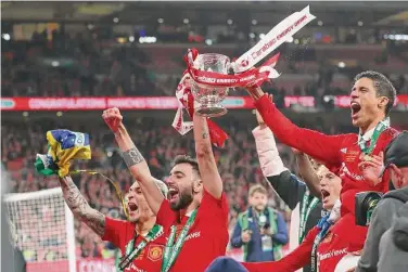  ?? Scott Heppell/Associated Press ?? Manchester United’s Bruno Fernandes holds the trophy aloft as he celebrates with teammates after winning the English League Cup final against Newcastle United on Sunday.