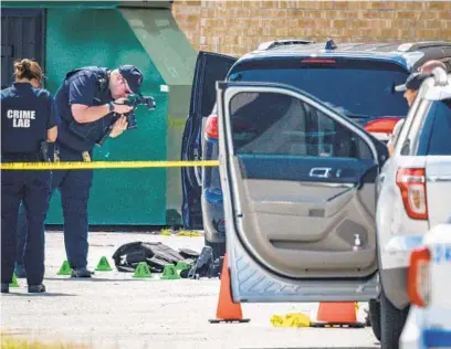 ?? JERRY JACKSON/BALTIMORE SUN ?? A crime lab technician takes photos of body armor and evidence markers in the Security Square Mall parking lot where a suspect was fatally shot by police after he shot and injured two Baltimore officers who were attempting to arrest him.