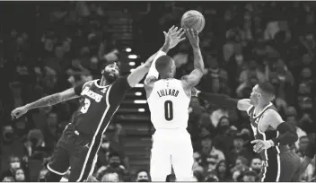  ?? STEVE DYKES/AP ?? PORTLAND TRAIL BLAZERS GUARD DAMIAN LILLARD (center) hits a 3-point shot from between Los Angeles Lakers Anthony Davis (left) and guard Russell Westbrook during the first half of a game in Portland, Ore. on Saturday.