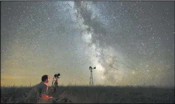  ?? TRAVIS HEYING/THE WICHITA EAGLE VIA AP ?? Omaha photograph­er Lane Hickenbott­om takes pictures of the night sky in July 2014 in a pasture near Callaway, Neb. With no moon in the sky, the Milky Way was visible to the naked eye.