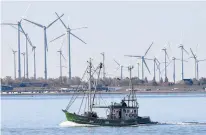  ?? MARTIN MEISSNER/AP 2019 ?? A fishing boat passes wind turbines on the North Sea coast of Germany. Four European Union countries plan to boost offshore wind capacity tenfold by 2050.