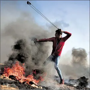  ?? AP/KHALIL HAMRA ?? A Palestinia­n protester slings a stone at Israeli soldiers Saturday during a clash near the border of Israel and the Gaza Strip. The soldiers responded with live fire and tear gas.