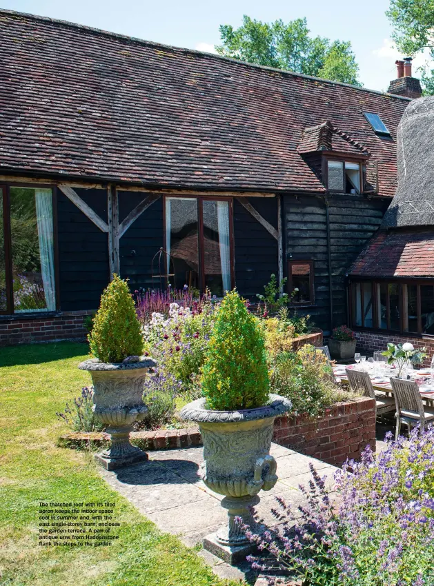  ??  ?? The thatched roof with its tiled apron keeps the indoor space cool in summer and, with the east single-storey barn, encloses the garden terrace. A pair of antique urns from Haddonston­e flank the steps to the garden